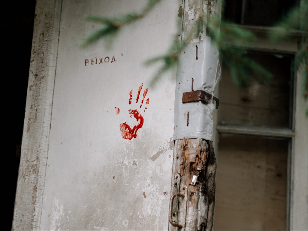 an old, beat up white door with a red hand print on it