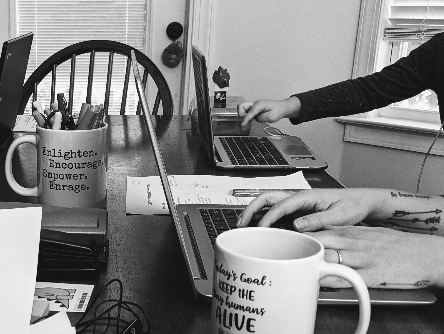 a table crowded with laptops, coffee mugs and papers