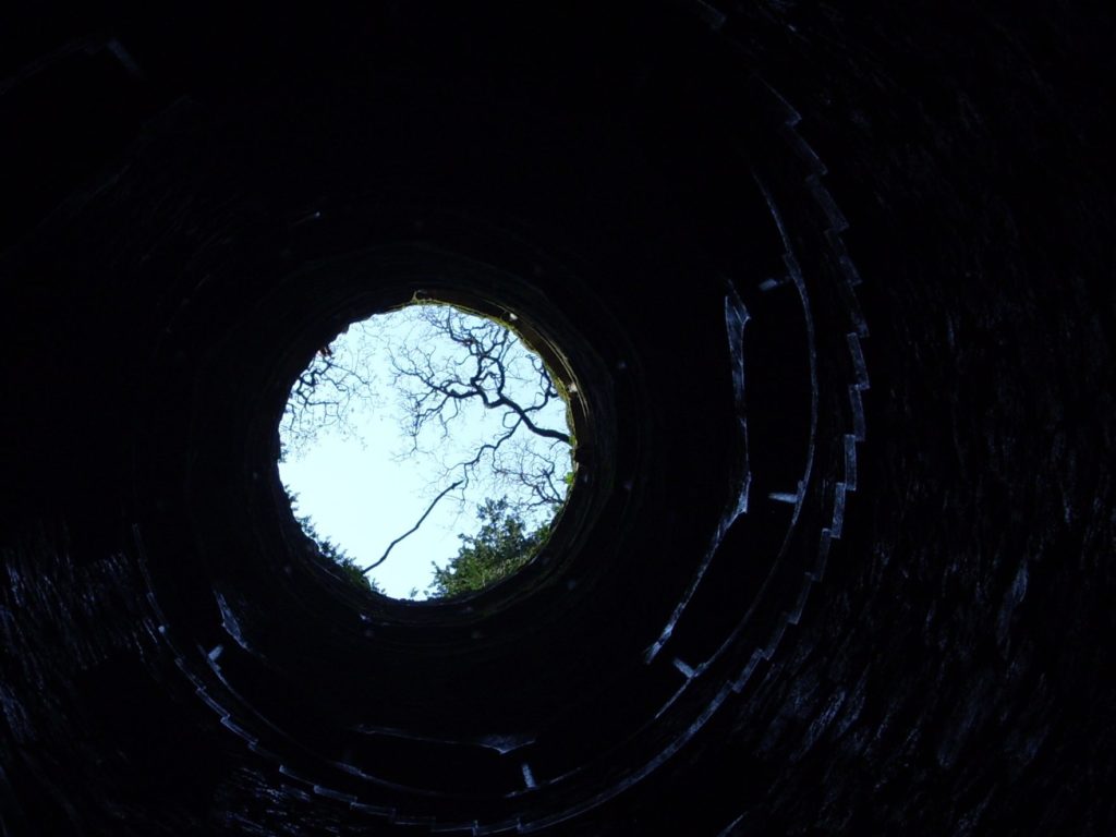 a dark well with an opening that shows the sky