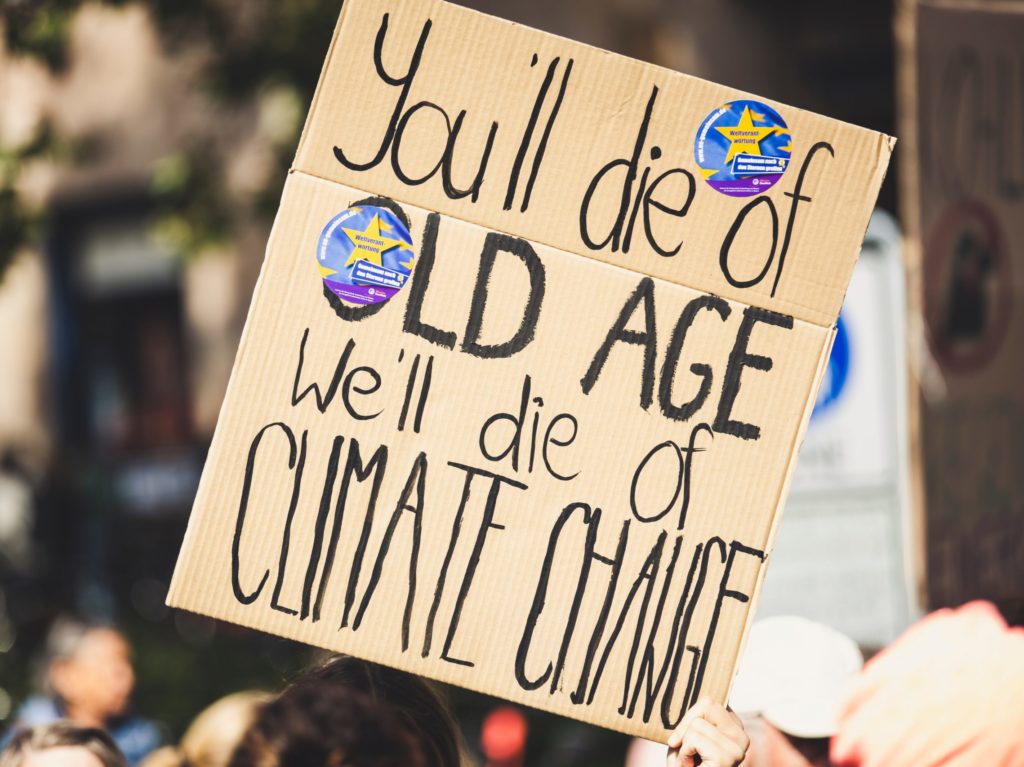 cardboard sign that reads, "You'll die of old age. We'll die of climate change."